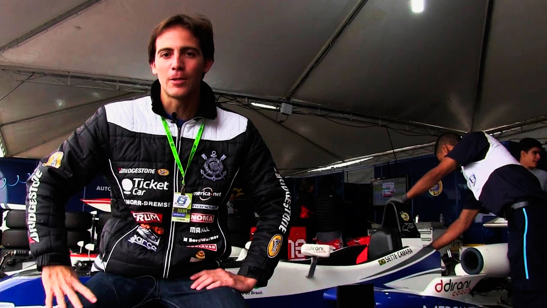 Danili Dirani, campeão de kart, sentado em cima de um carro de formula 1, como se estivesse conversando com a câmera.