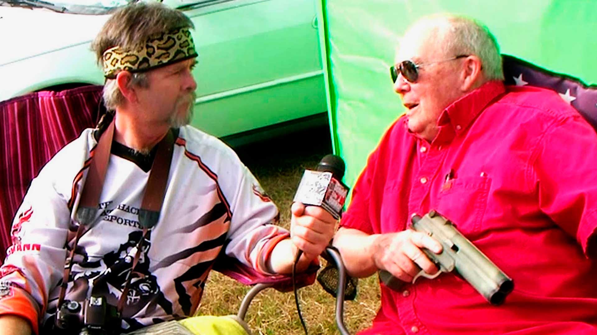 Imagem do Bob Gurnsey, criador do paintball, dando entrevista. Em sua mão ele segura uma pistola.