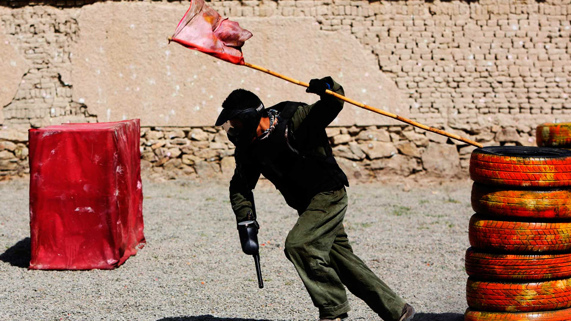 Jogador de paintball correndo com a arma de paintball em uma mão e na outra a bandeira que capturou.