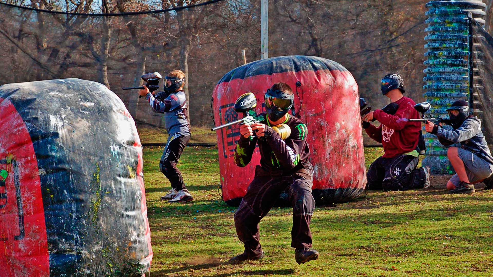 Campeonato de paintball. Na imagem aparece 4 pessoas do mesmo time, duas mais atrás, em posição defensiva, e duas pessoas avançando.