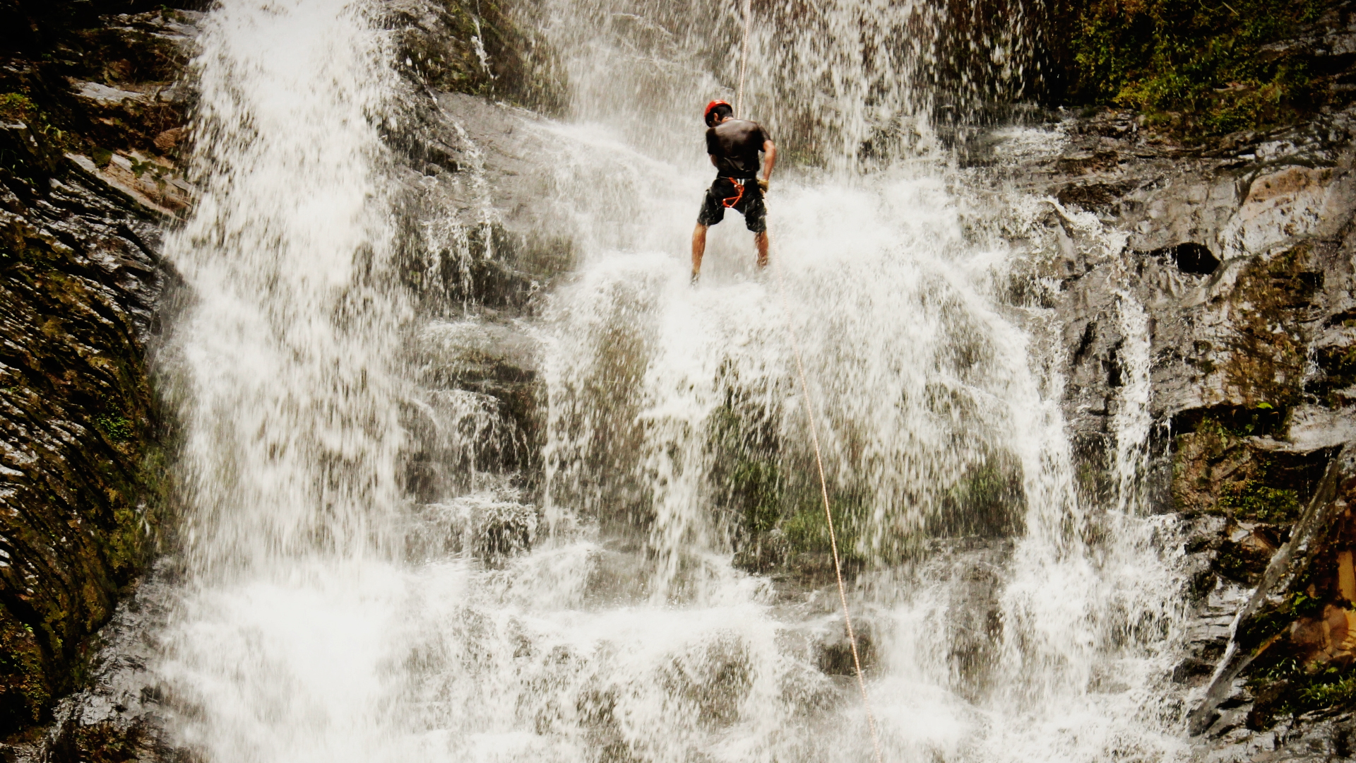 Homem praticando rapel em uma cachoeira.