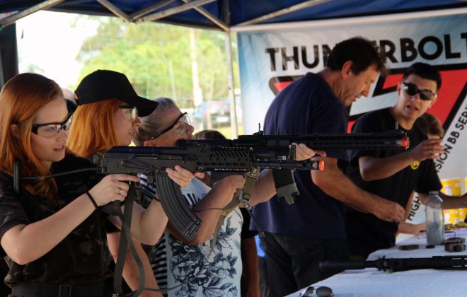 Na imagem há um estande de tiro, com três mulheres segurando armas de airsoft, prontas para atirar.