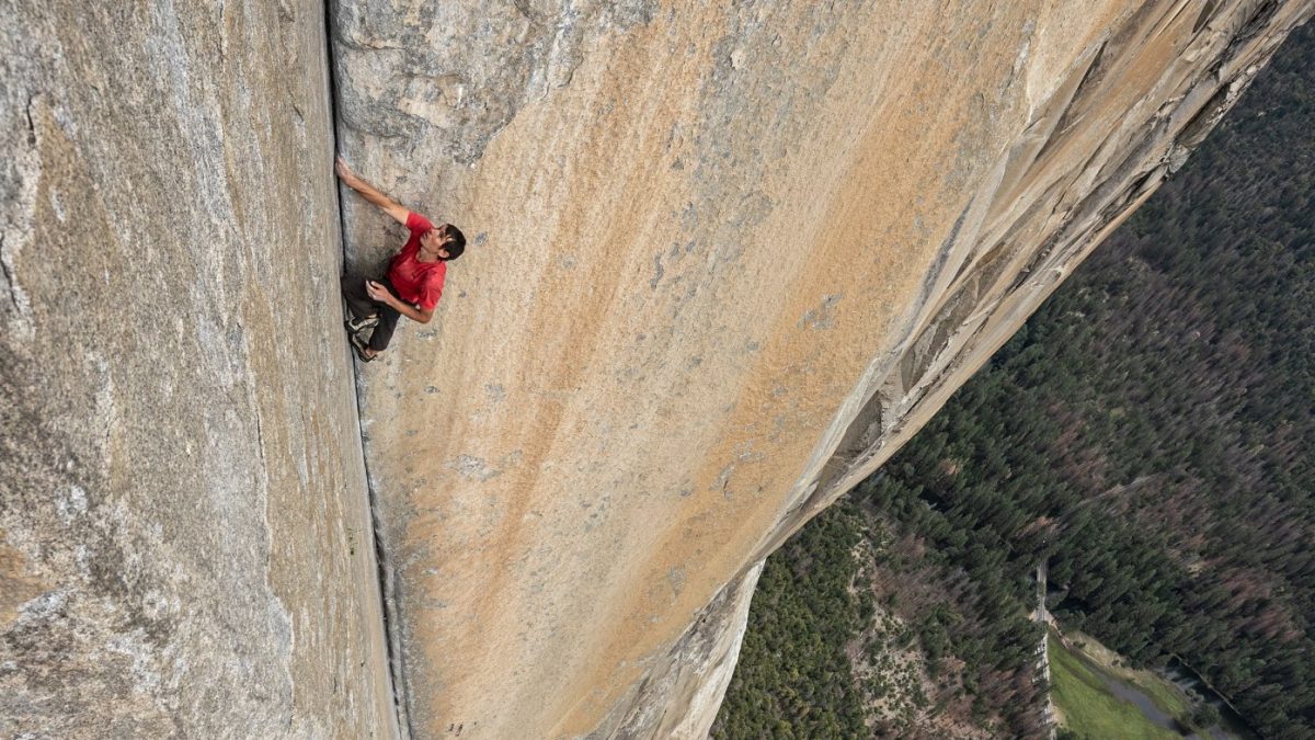 Na imagem, Alex aparece escalando um paredão enorme. O alpinista está com as mãos entre uma abertura da rocha.