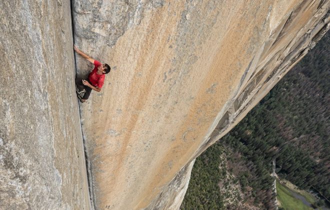 Na imagem, Alex aparece escalando um paredão enorme. O alpinista está com as mãos entre uma abertura da rocha.