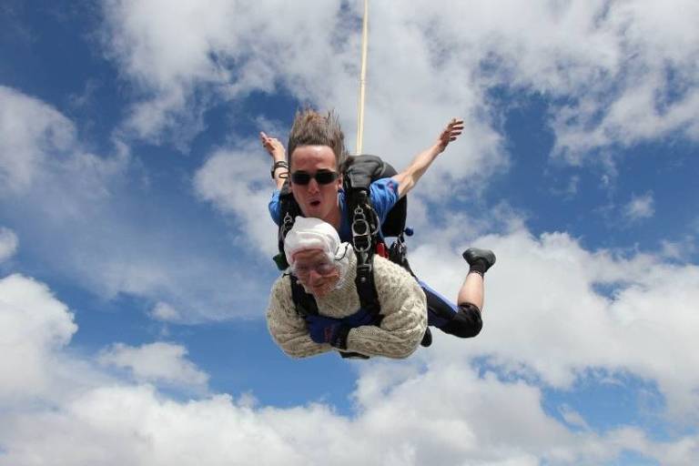 Na imagem, uma senhora de 102 anos está no meio do seu salto de paraquedas, com o instrutor atrás dela.