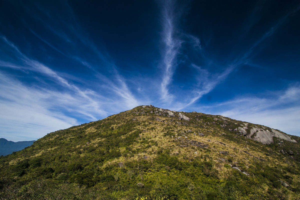 Na imagem, temos o pico do Morro do Anhangava. Ao fundo, uma paisagem de céu muito azul e iluminado.