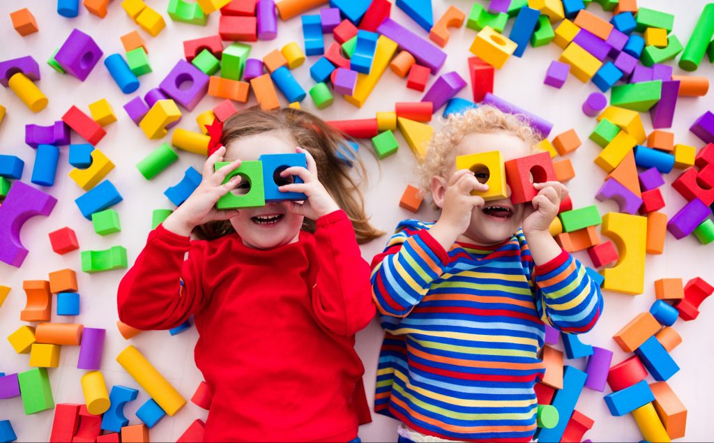 Duas crianças felizes brincam com blocos coloridos de construir brinquedos. 