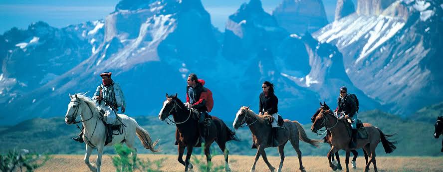 Na imagem, quatro homens montado em cavalos e se posicionam em fila indiana, um atrás do outro.