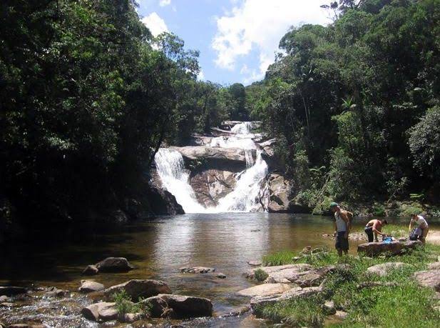 Na imagem há uma pequena cachoeira que forma uma piscina natural com pedras.